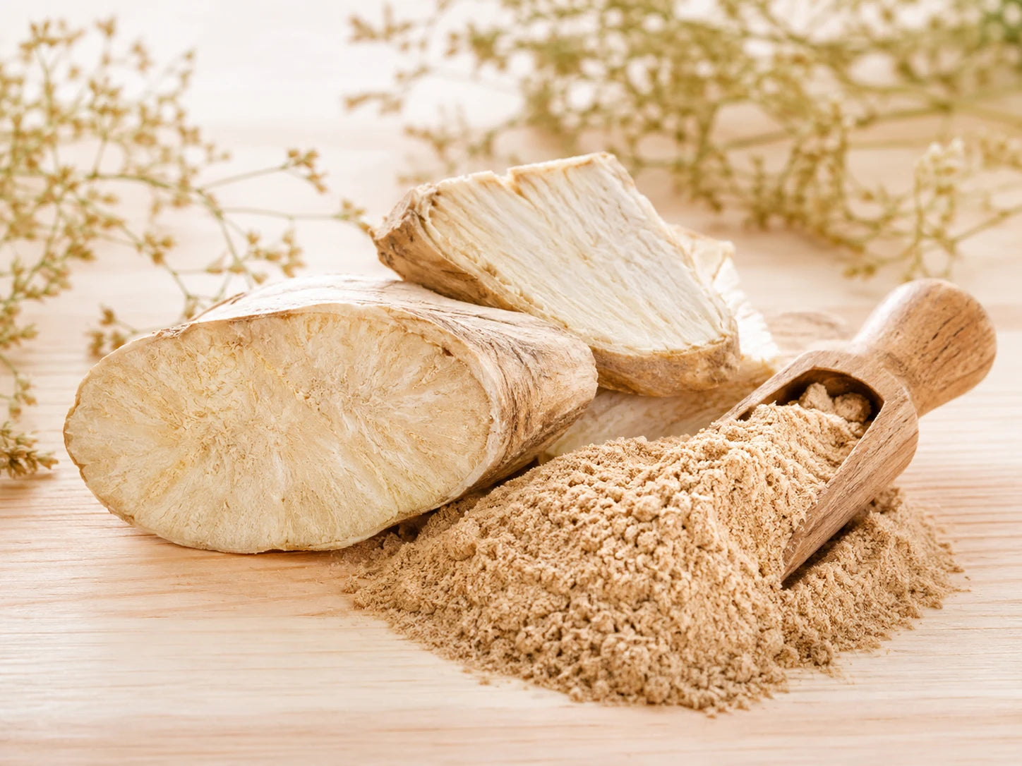 Cut pale kudzu root pieces beside a pile of pale fawn root powder on a warm wood surface with dried sprigs behind